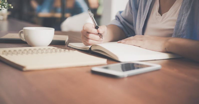 Personalized Learning - Woman Writing on a Notebook Beside Teacup and Tablet Computer