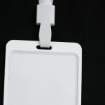 E-learning Security - Plastic name tag with white ribbon and blank paper hanging on black background