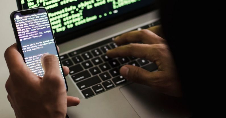Malware Evolution - Unrecognizable hacker with smartphone typing on laptop at desk